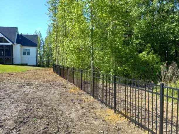 A black fence surrounds a dirt field in front of a house.