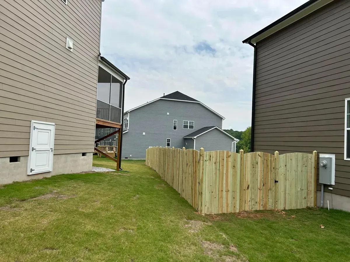 A wooden fence surrounds a lush green yard between two houses.