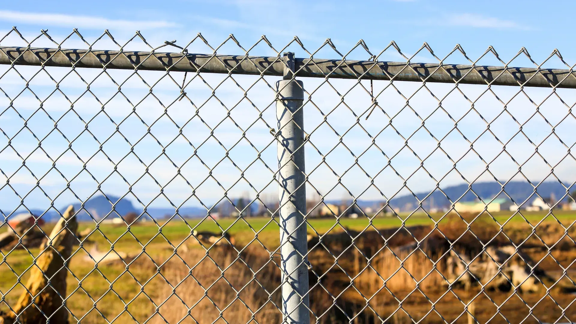A close up of a chain link fence with a field in the background.