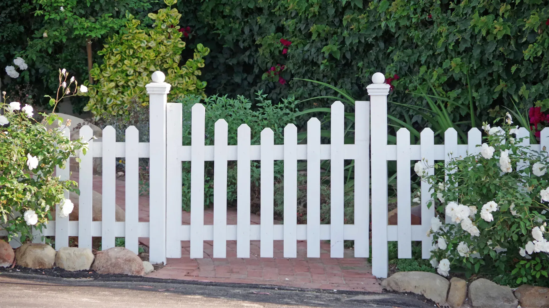 A white picket fence surrounds a garden with white flowers