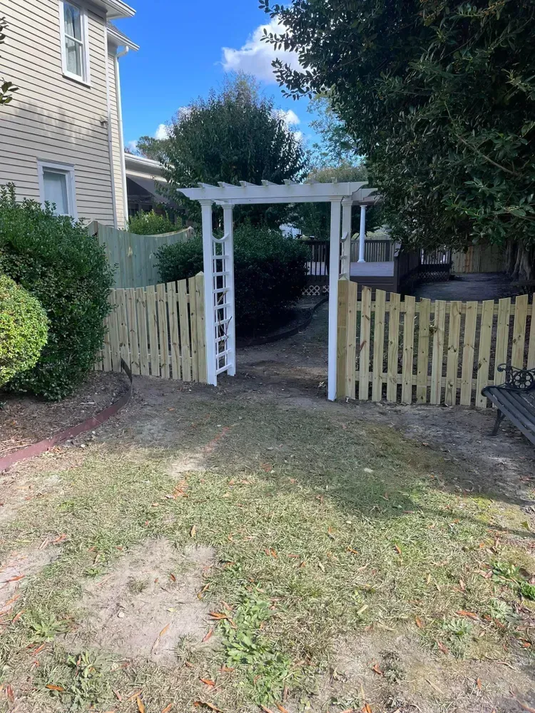 A wooden fence with a pergola in the backyard of a house.