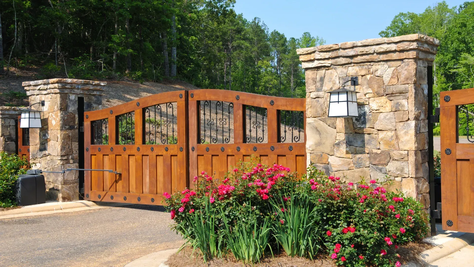 A wooden gate is surrounded by stone pillars and flowers