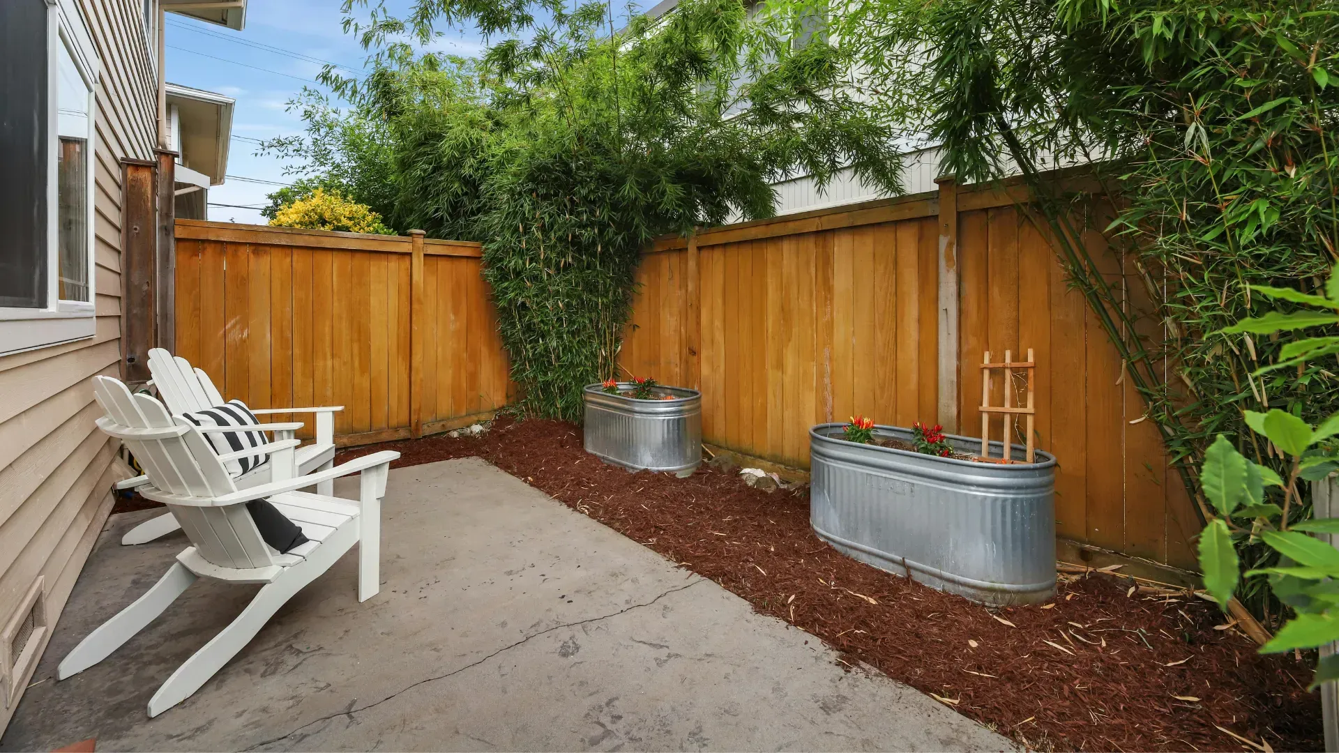 There are two chairs in the backyard with a wooden fence.