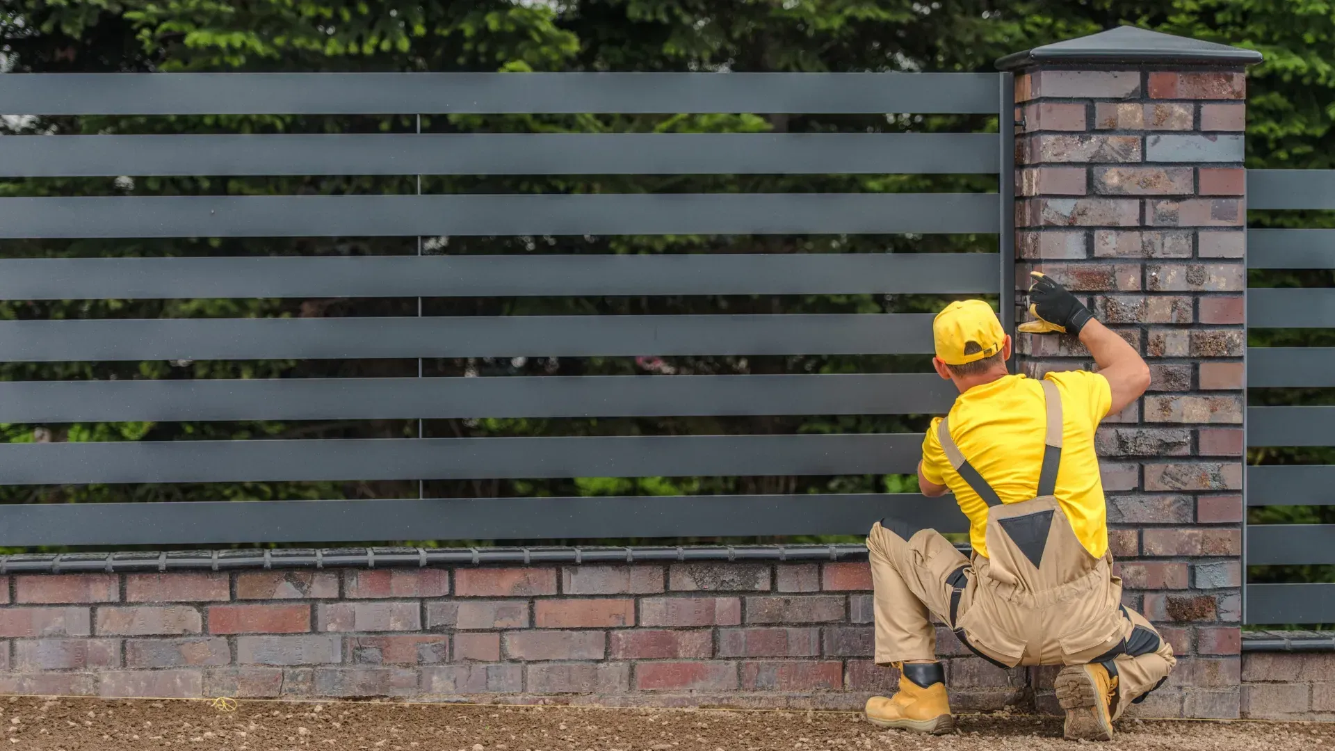 A man is installing a fence on a brick wall.