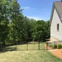 A house with a fence around it and a large lawn in front of it.