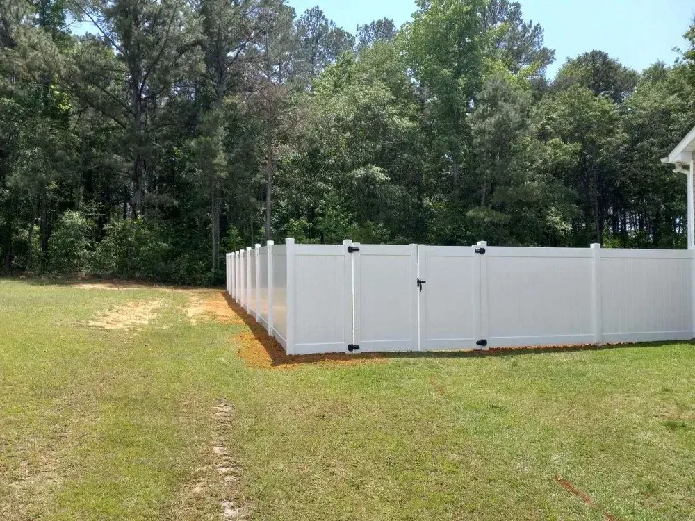 A white fence with a gate is in the middle of a grassy field.