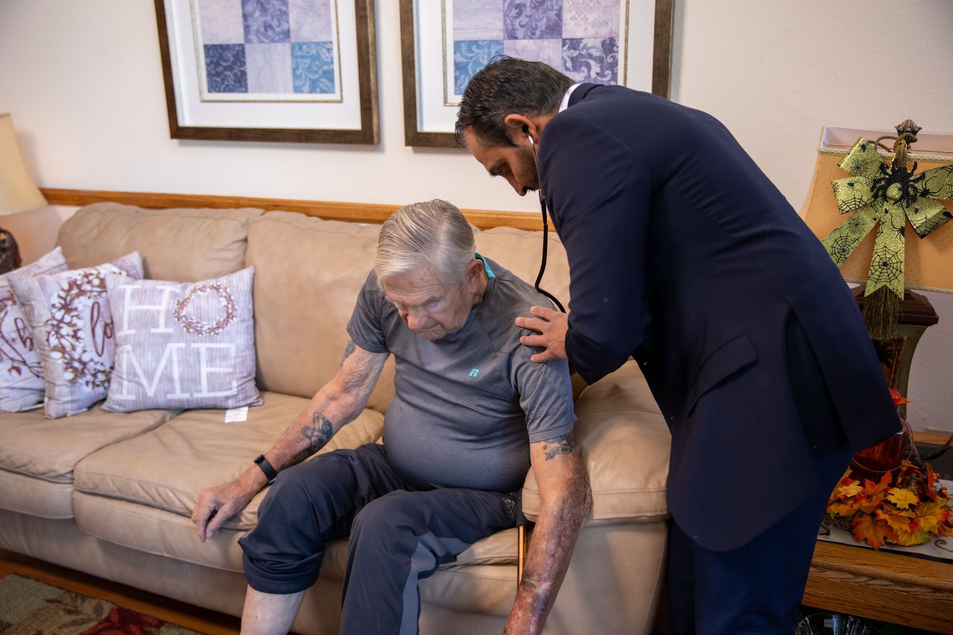 A man in a suit is taking a man 's heartbeat with a stethoscope.