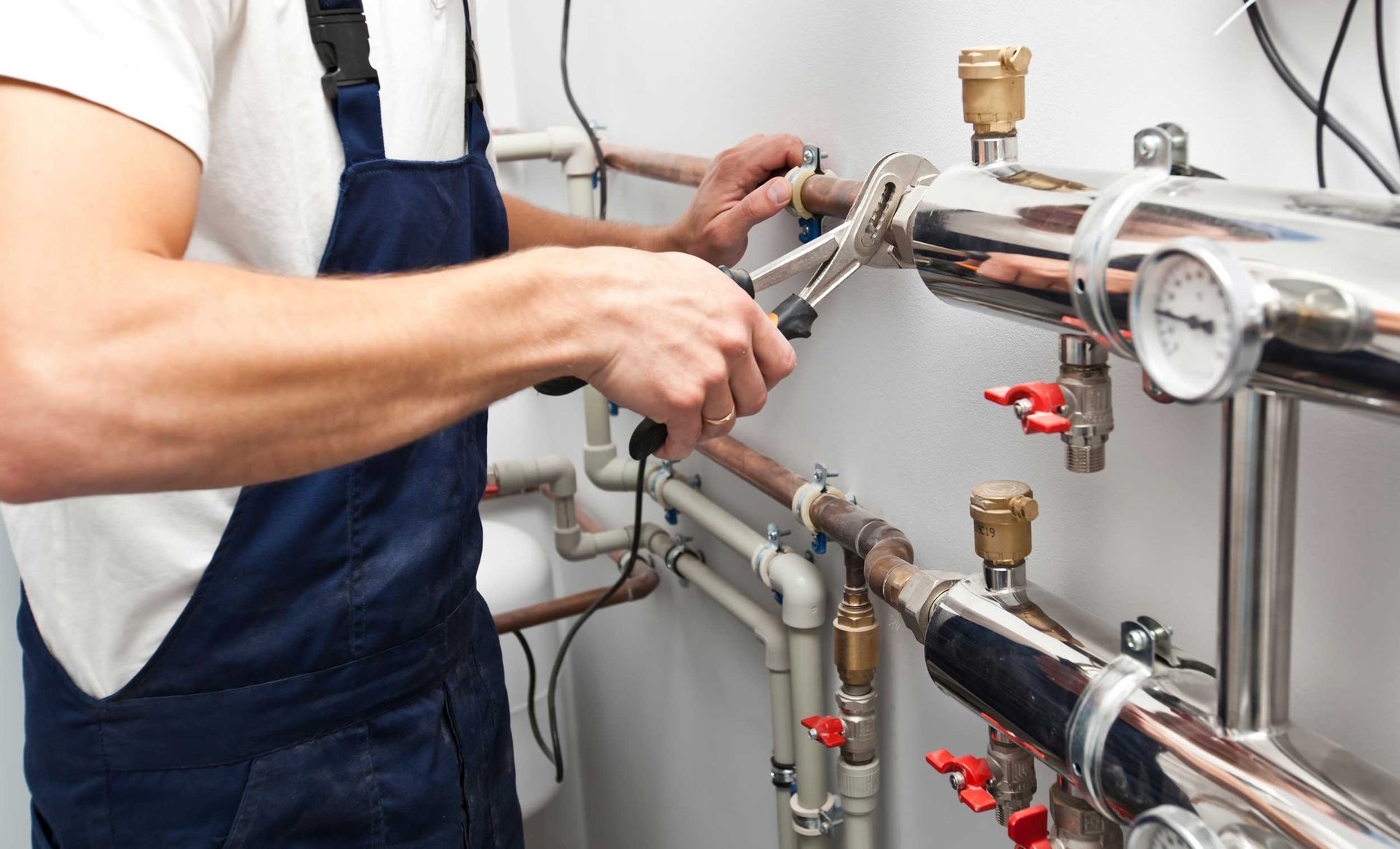 Plumber tightens pipe fittings and valves on a commercial plumbing system using hand tools.