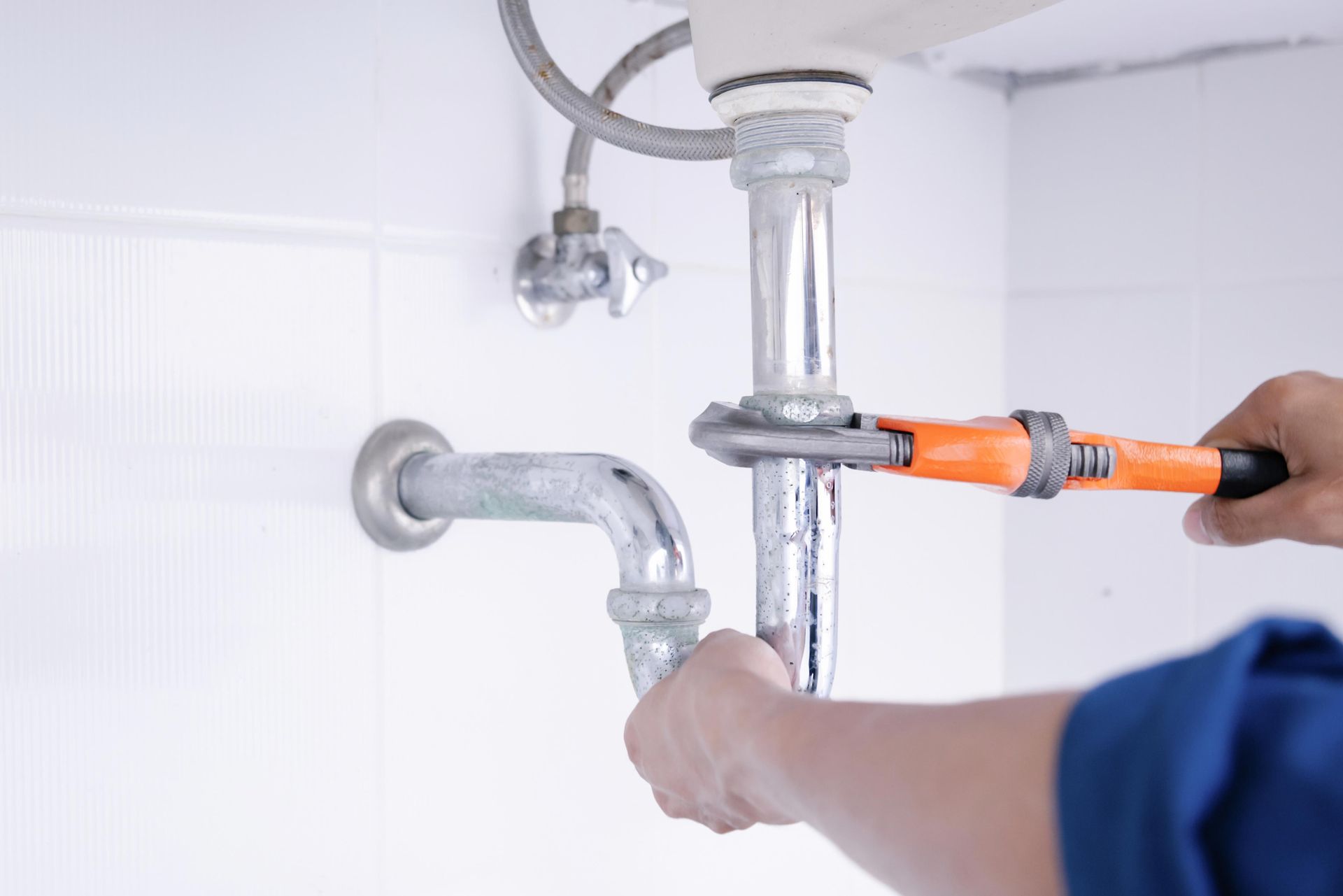 Plumber tightening a metal pipe under a sink using an adjustable wrench.