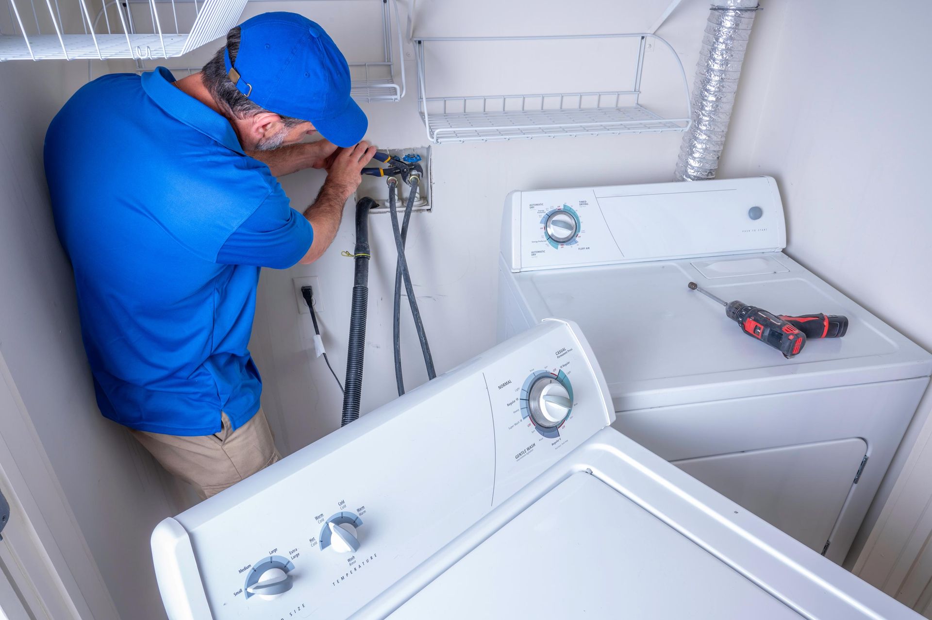 Plumber installing water supply lines behind a washing machine in a laundry room.