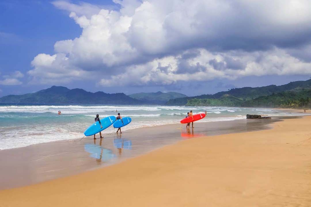 Two people are carrying surfboards on a beach.