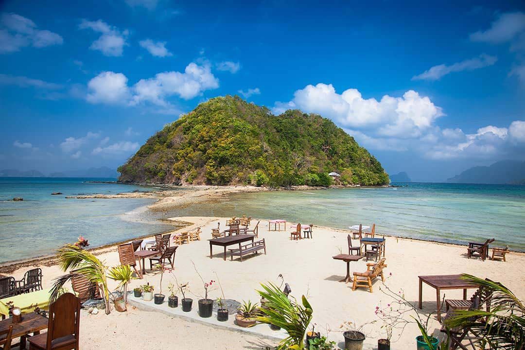 A small island in the middle of the ocean with tables and chairs on it.