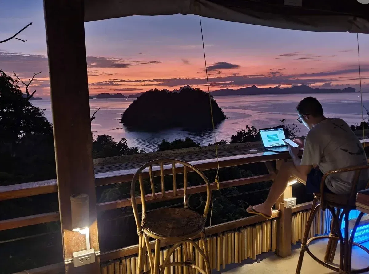 A man is sitting on a balcony using a laptop computer.