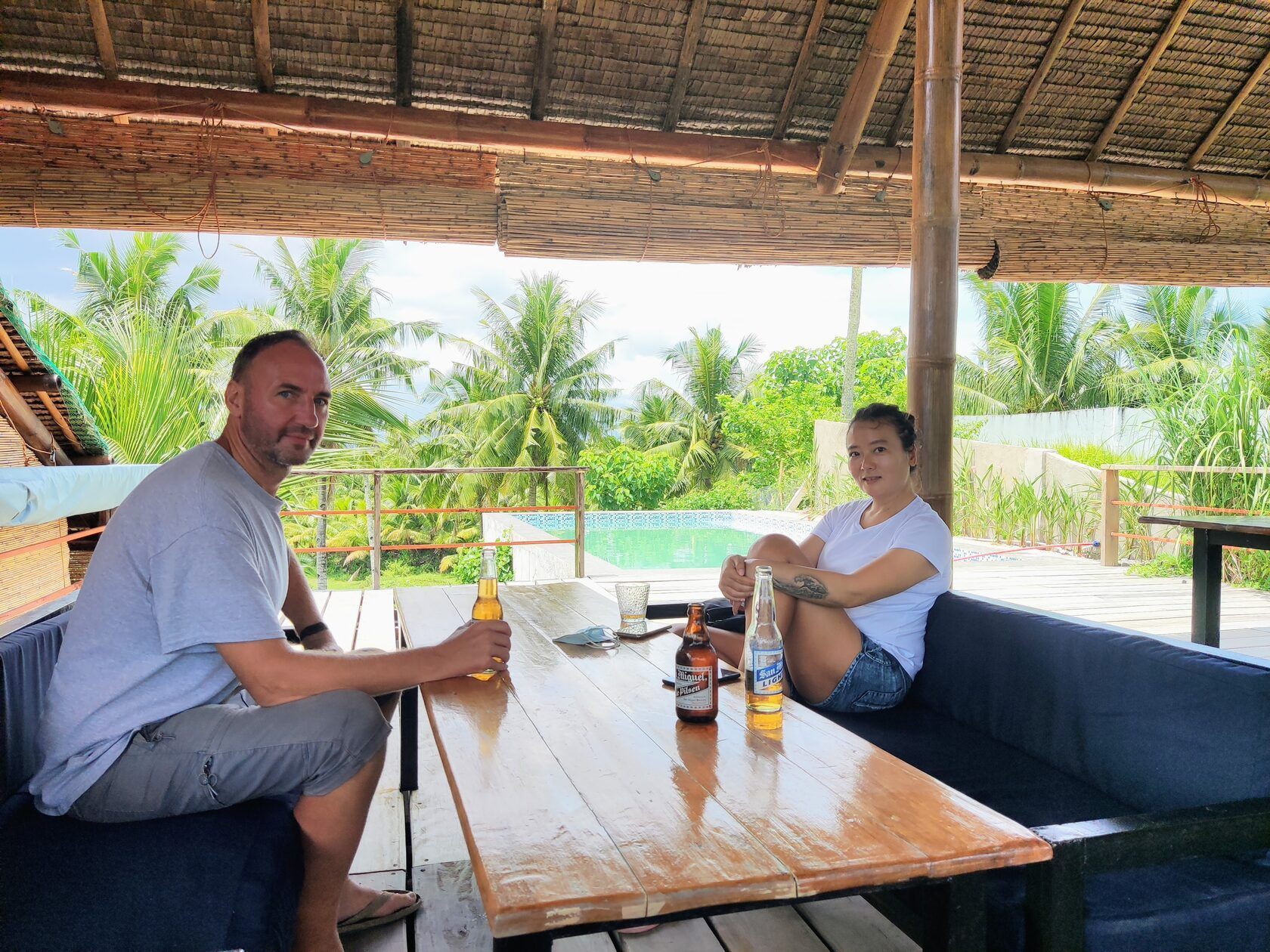 A man and a woman are sitting at a table with bottles of beer.