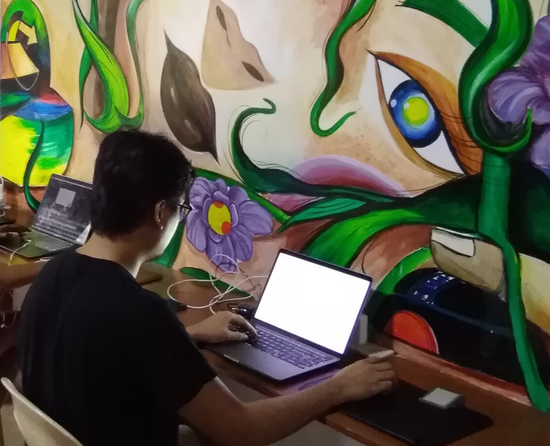 A man is using a laptop in front of a mural