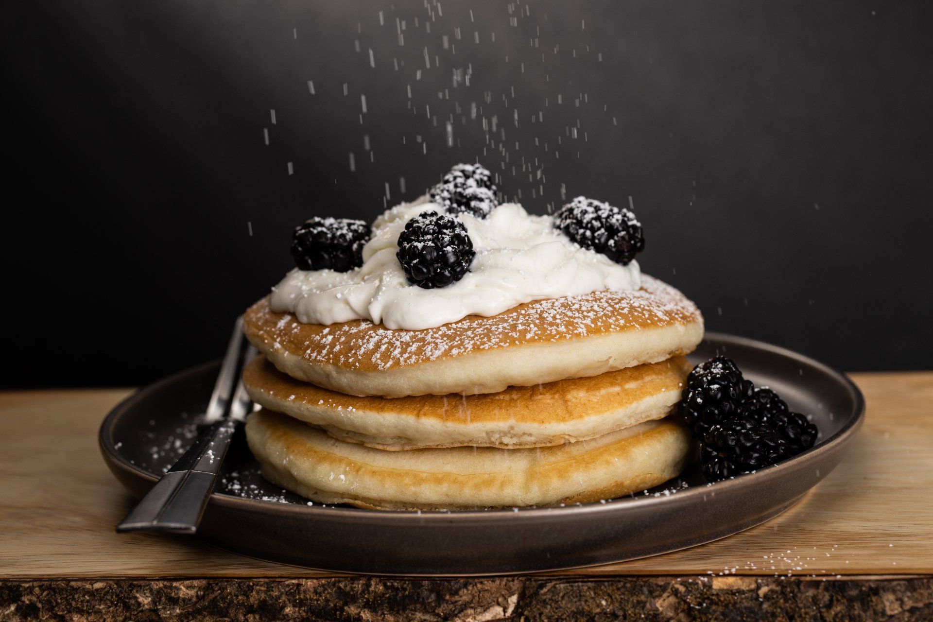 A stack of pancakes with whipped cream and blackberries on a plate.