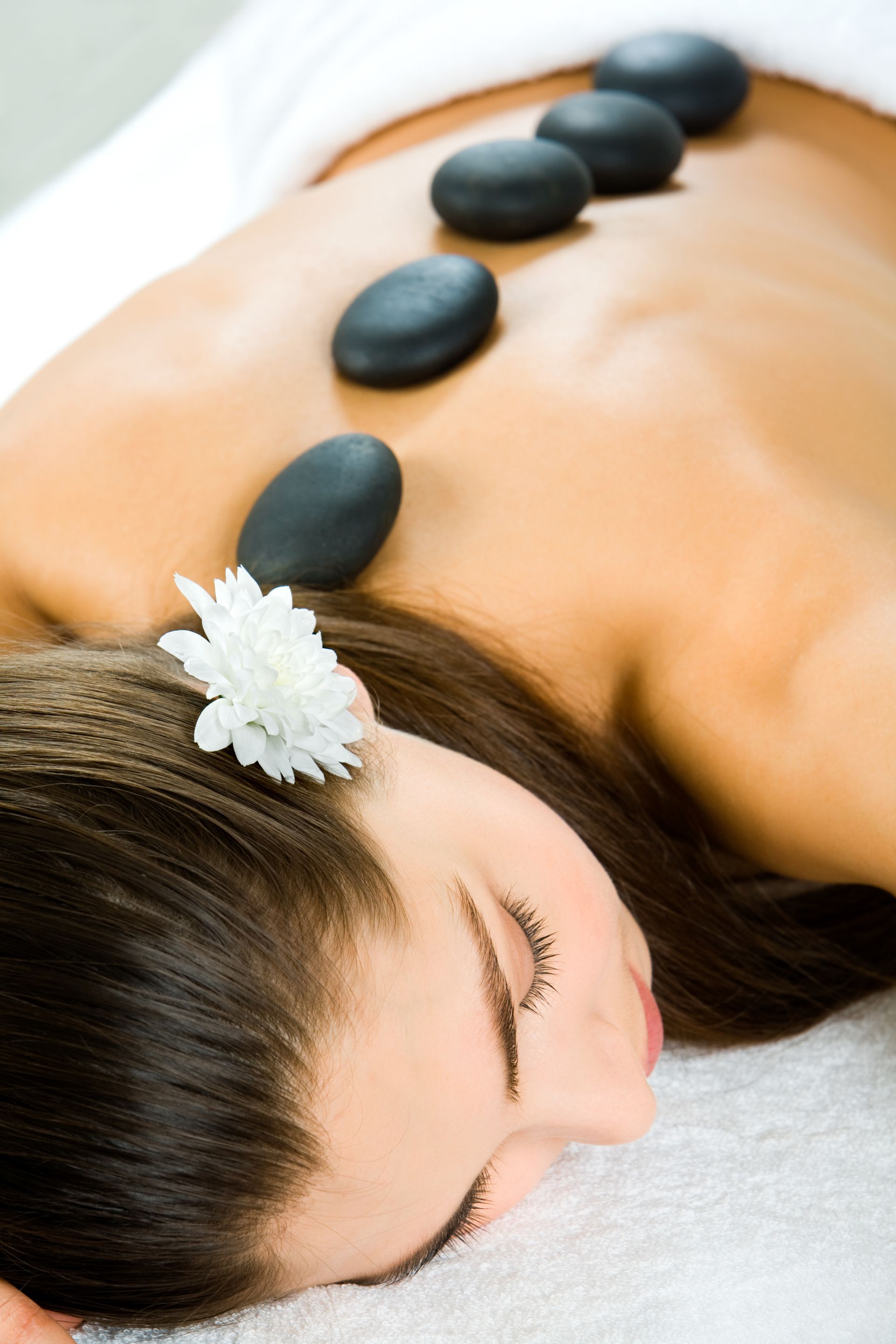 A woman is laying on a table with black rocks on her back.