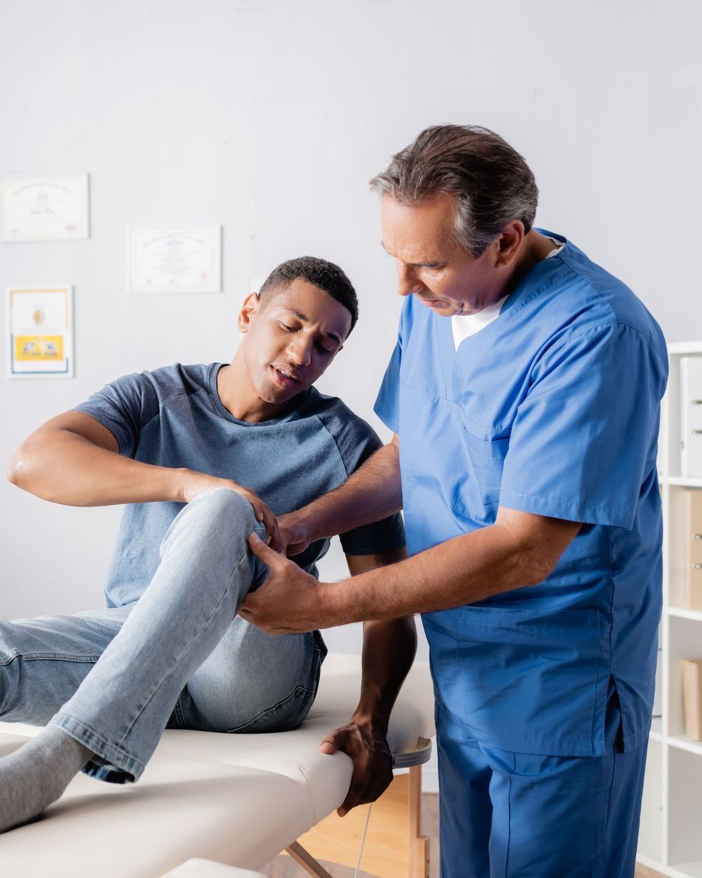 A man is sitting on a table while a doctor examines his leg.