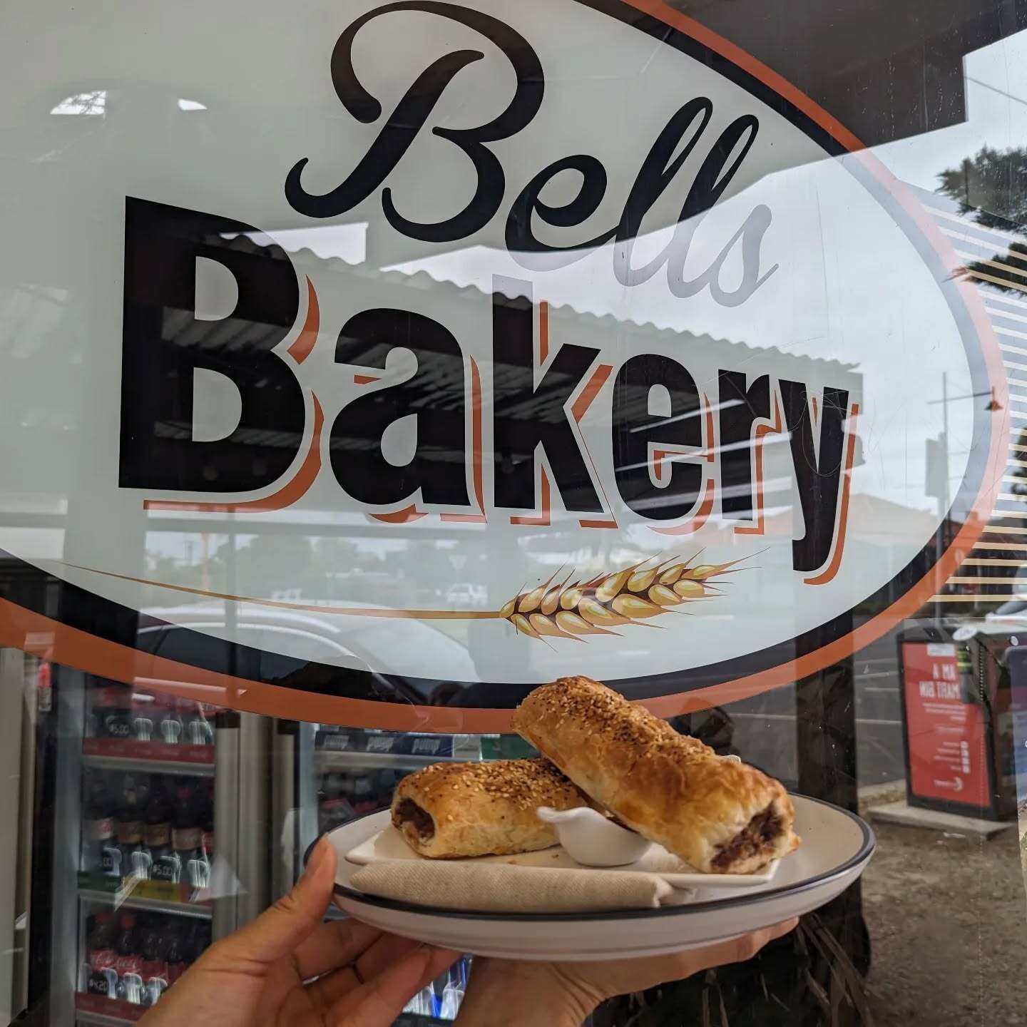 A person is holding a plate of food in front of a bell bakery sign