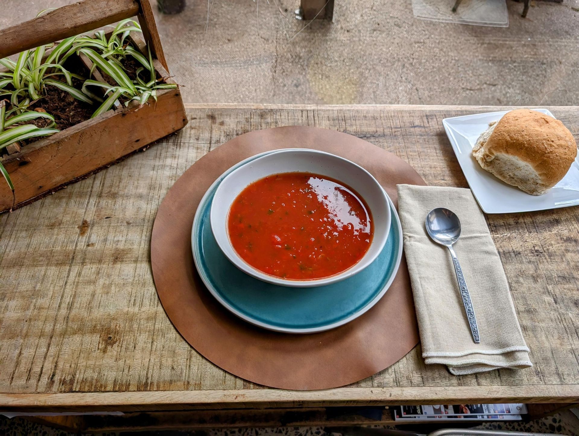 A bowl of tomato soup is on a table next to a plate of bread and a spoon.