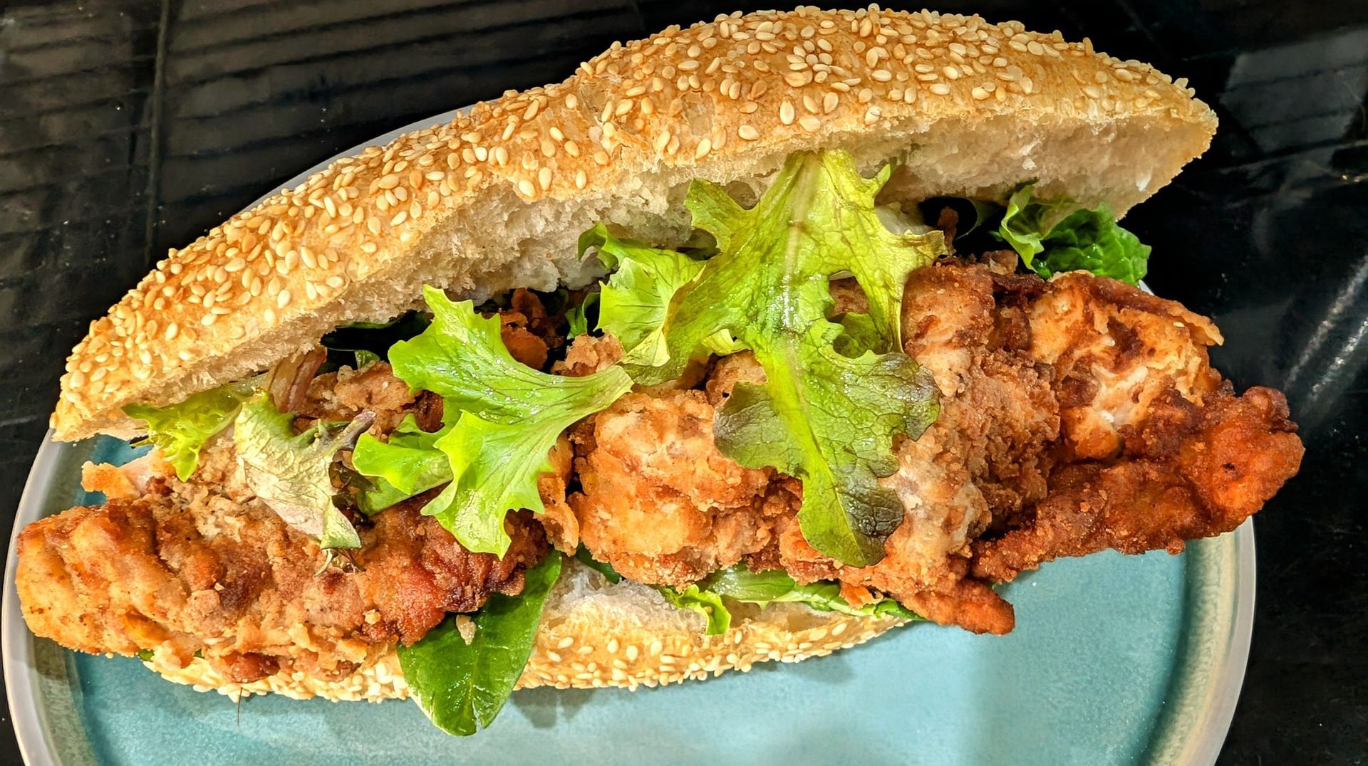 A fried chicken sandwich with lettuce on a sesame seed bun on a blue plate.