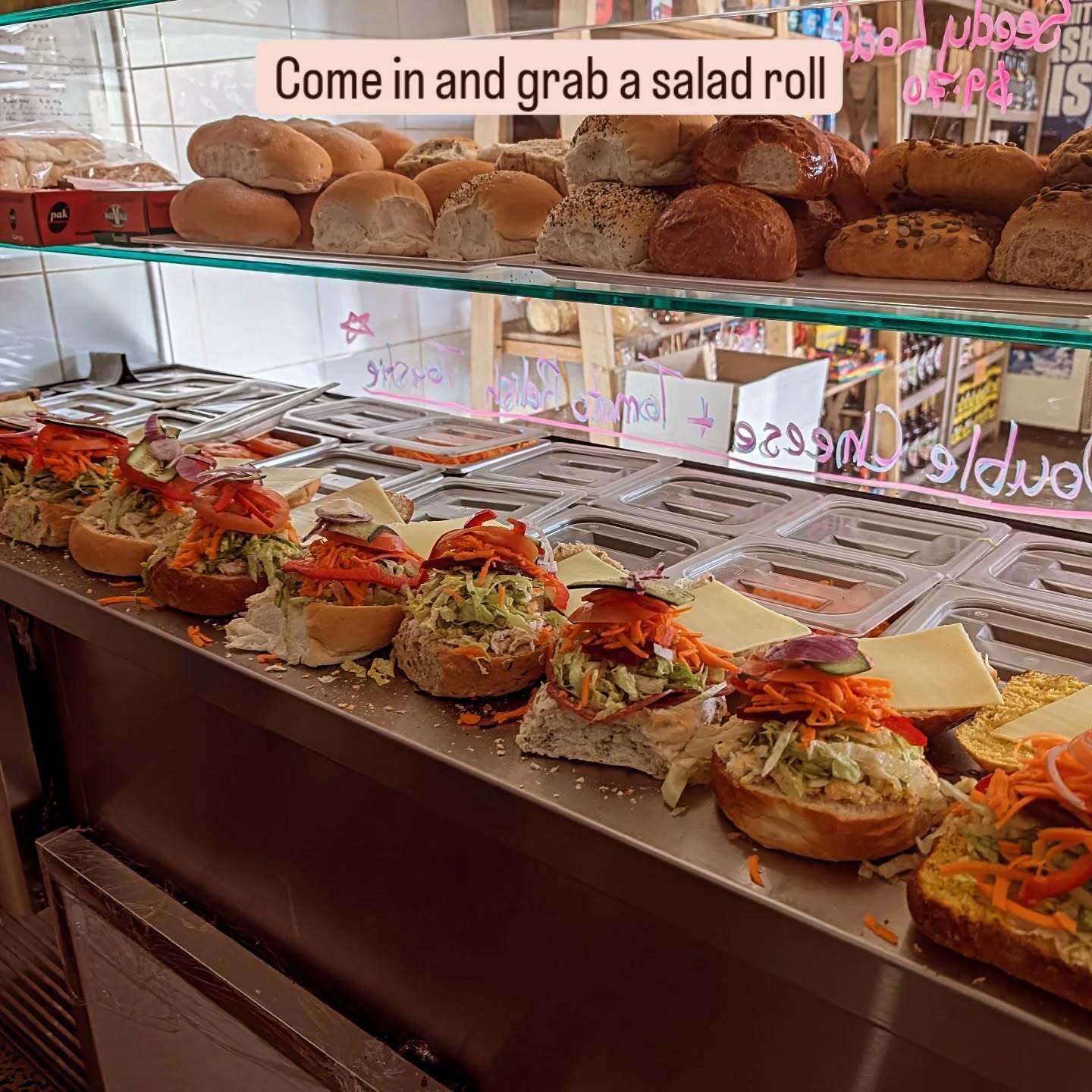 A display case filled with sandwiches and rolls with a sign that says come in and grab a salad roll.