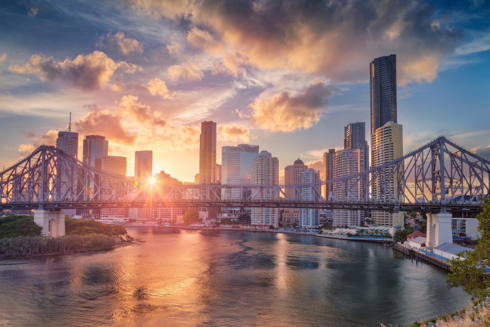 A Bridge Over a River with A City Skyline in The Background at Sunset — Creative Commercial Furniture in Brisbane, QLD