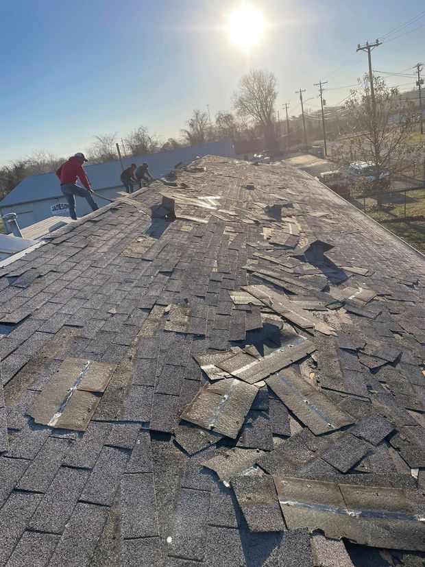 Rooftop covered in ice and snow under bright sun, with two people working near the left edge.
