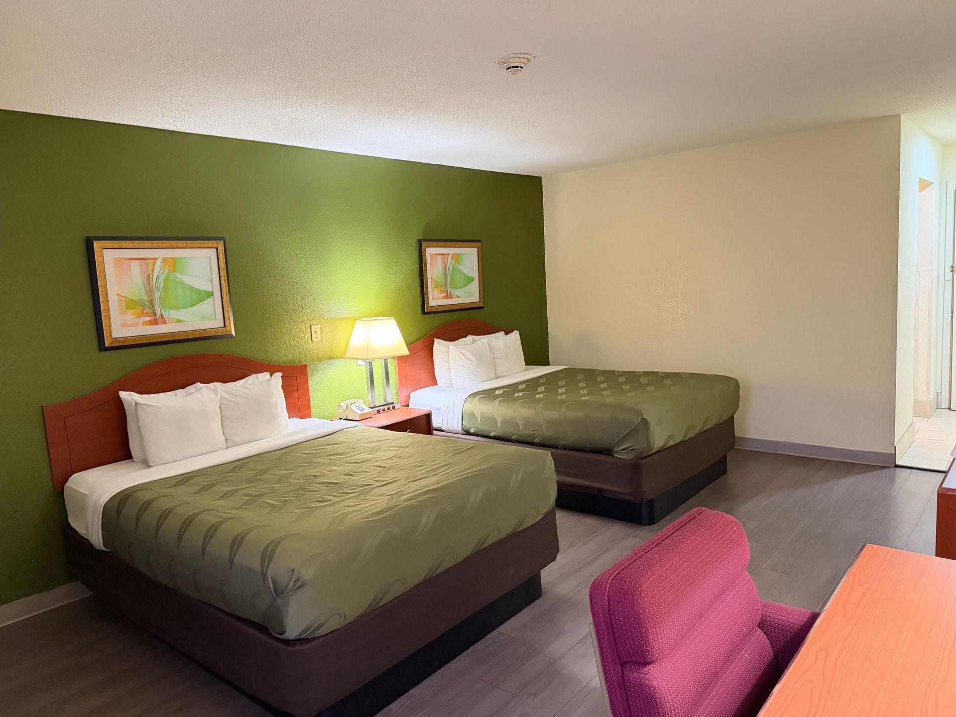 Hotel room with two queen beds, green walls, framed art, and a red chair.
