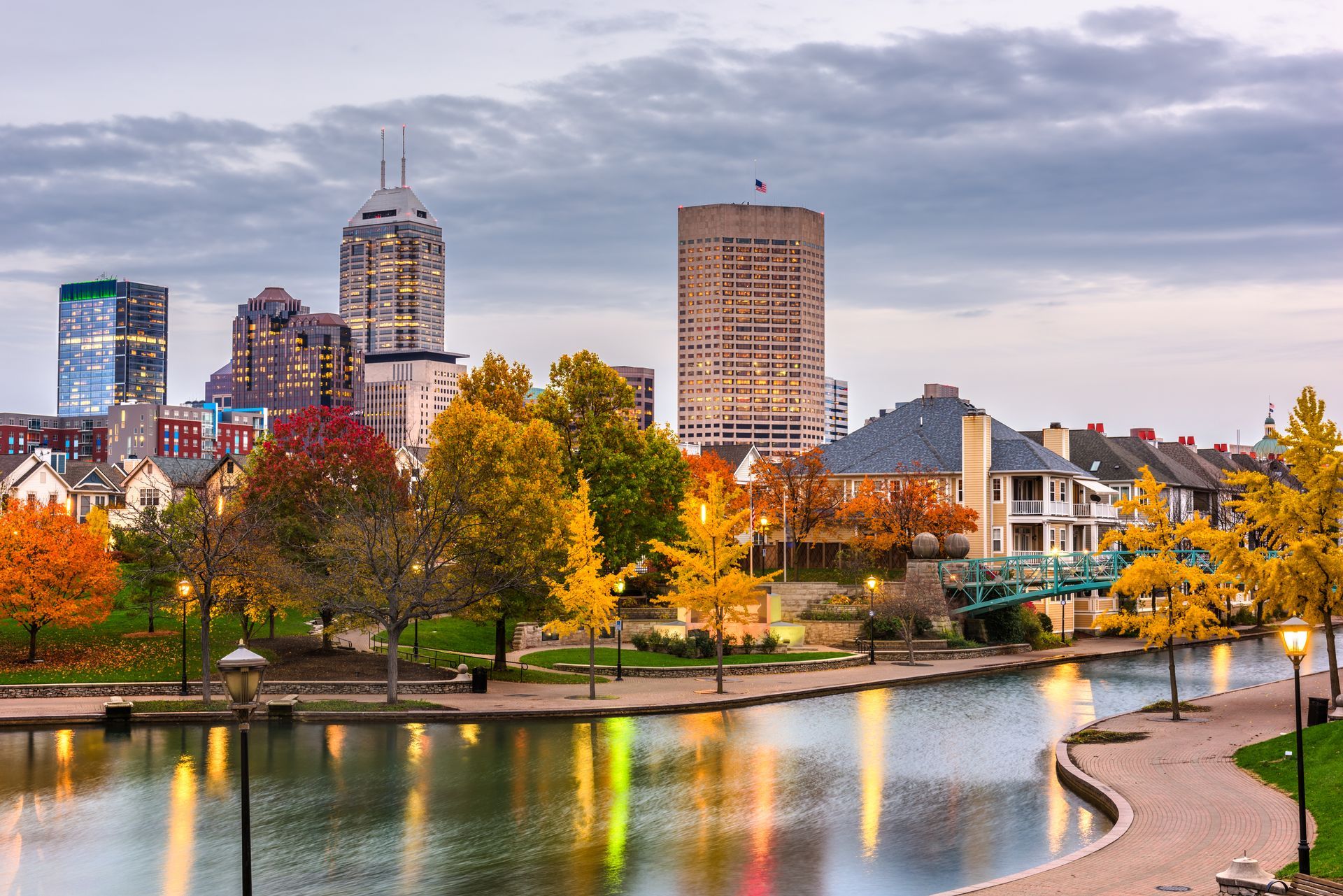 Indianapolis skyline over canal with fall foliage. Buildings reflect in water on cloudy day.