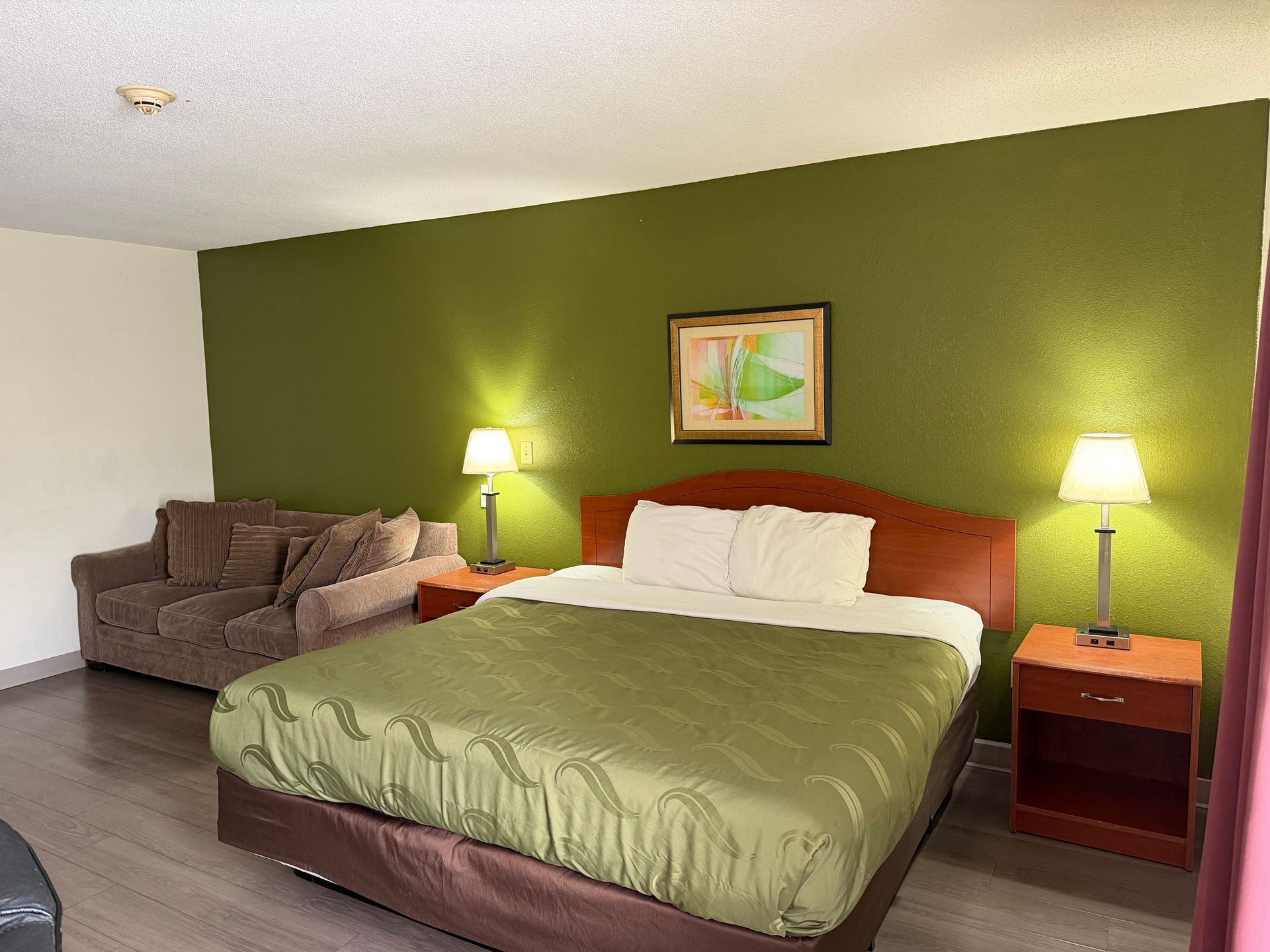 Hotel room with green accent wall, bed, sofa, and two lamps.