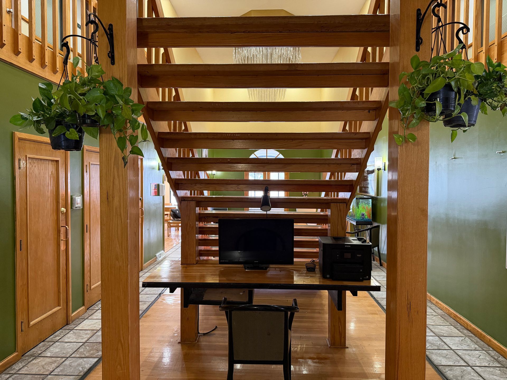 Wooden staircase with office setup underneath, plants hanging on either side, green walls.