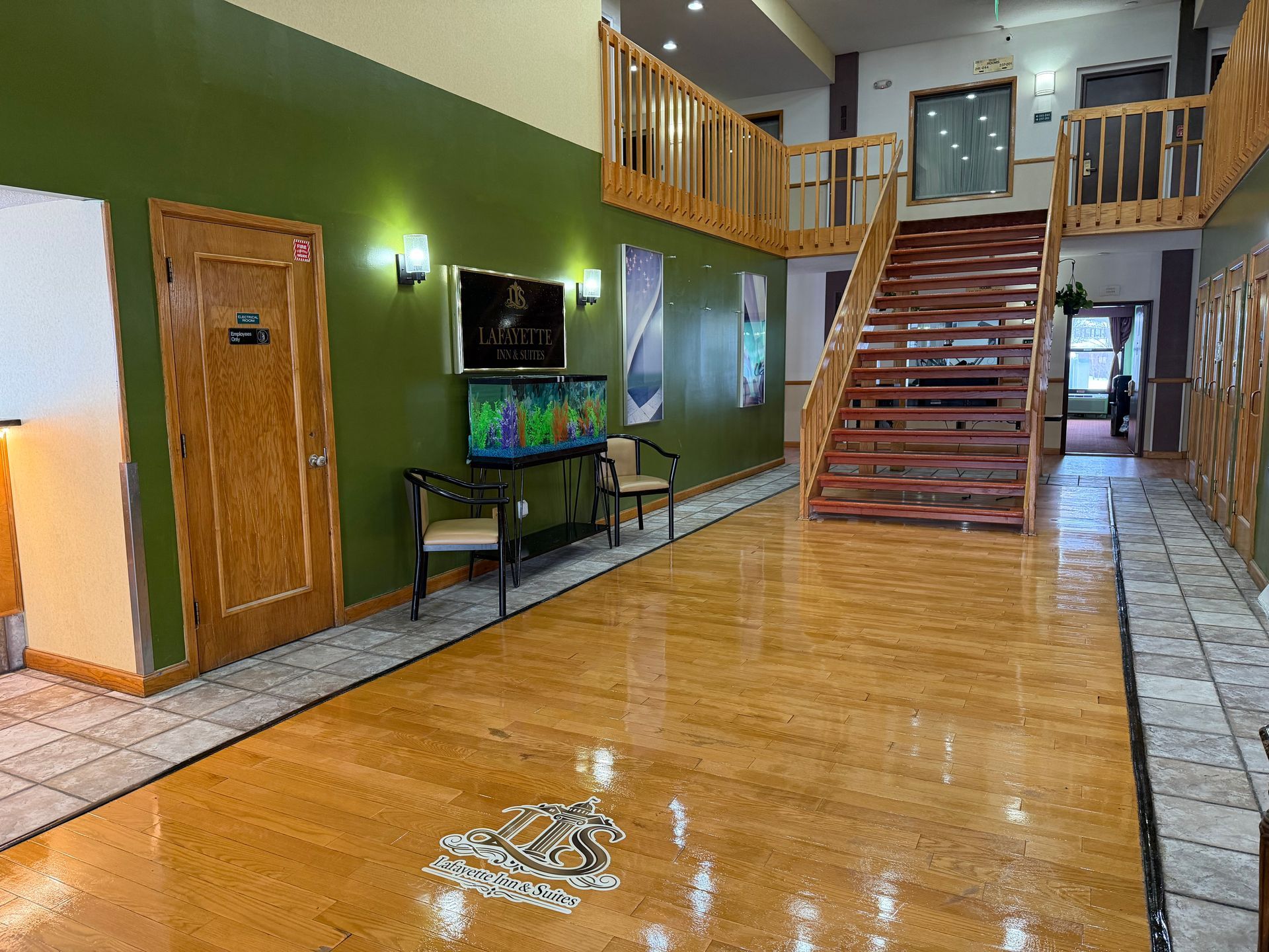 Wooden staircase in a large lobby with green wall, artwork, fish tank, and glossy wooden floor.