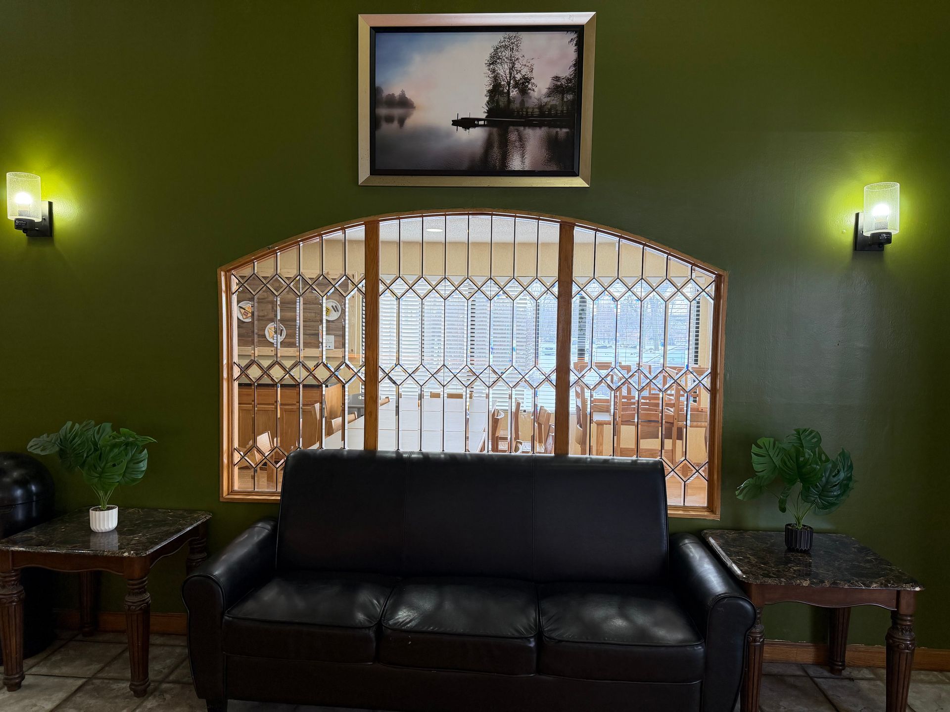 Green wall with a black couch, side tables, and a framed landscape above a window with a security gate.