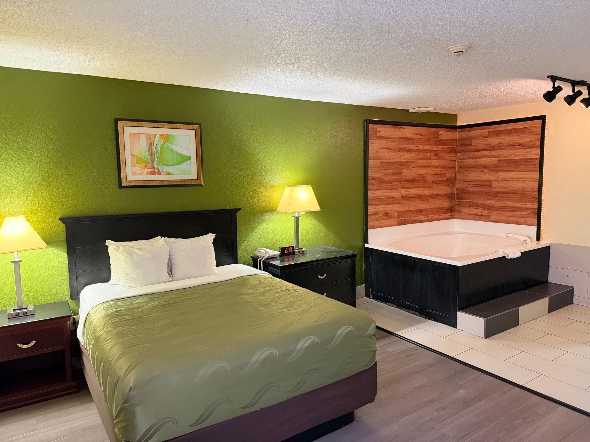 Hotel room with a bed, nightstands with lamps, a jacuzzi, and green walls.