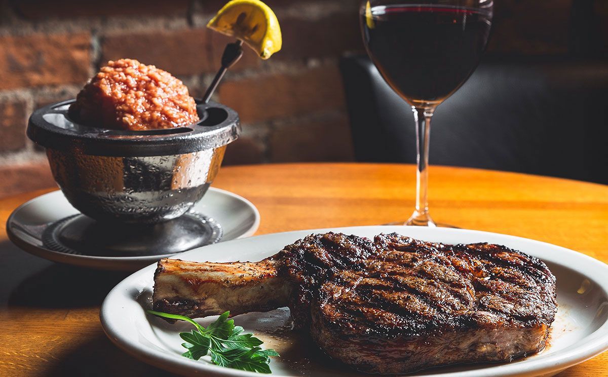 Grilled steak, butter, red wine, and lemon on a table in a restaurant setting.