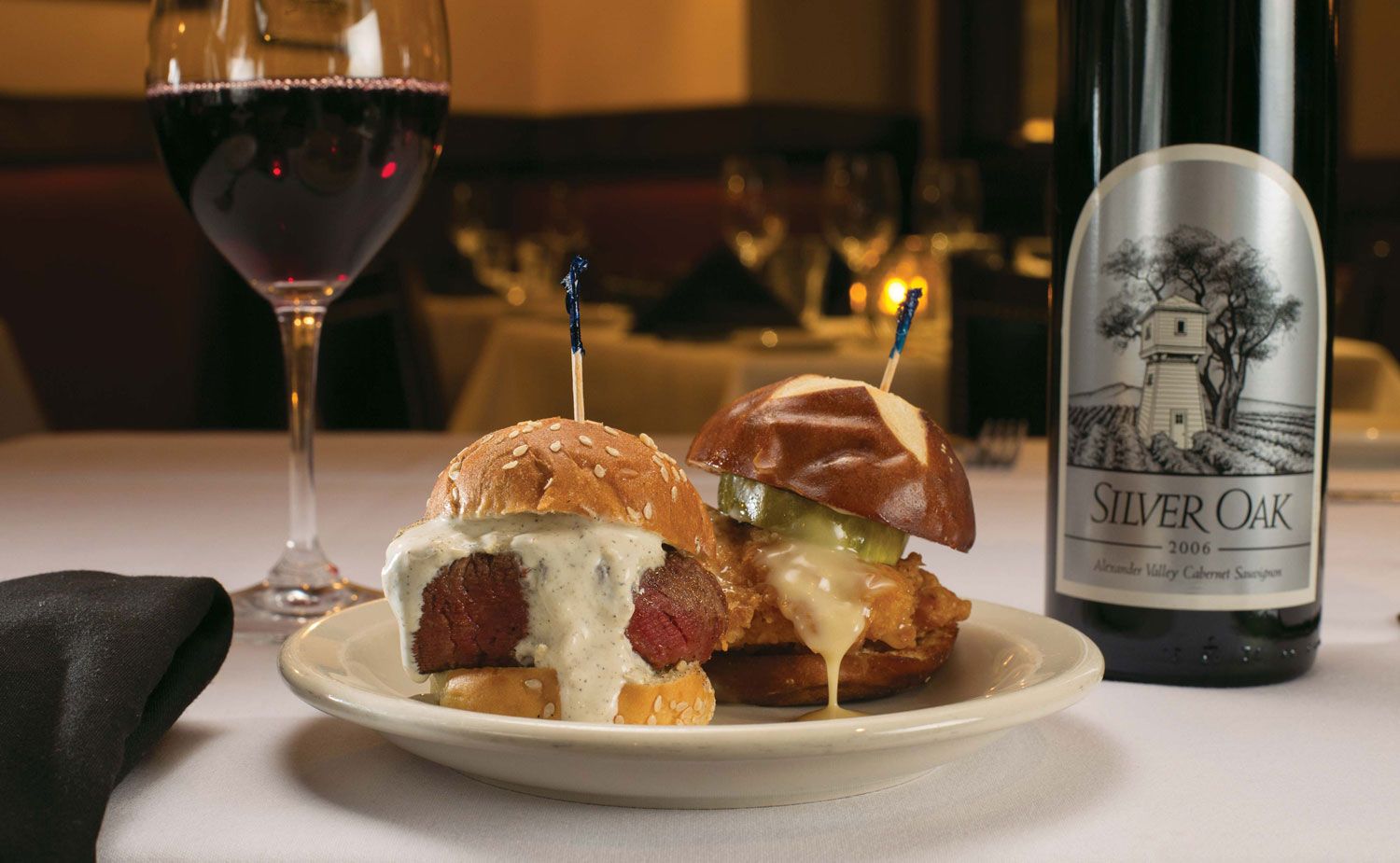 Two sliders on a plate with red wine and a Silver Oak wine bottle.