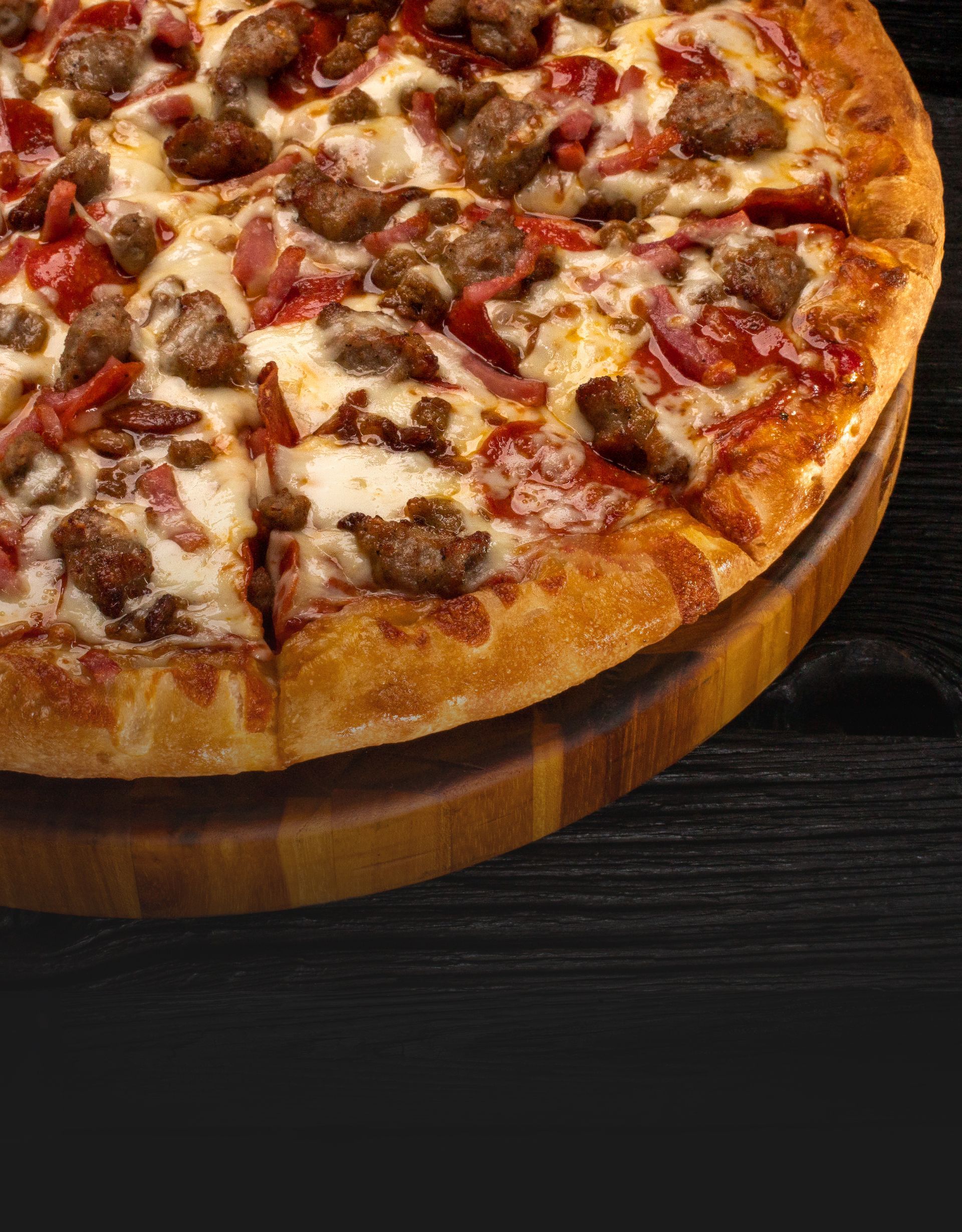 All-meat pizza topped with sausage, bacon, pepperoni, and ham on a wooden cutting board