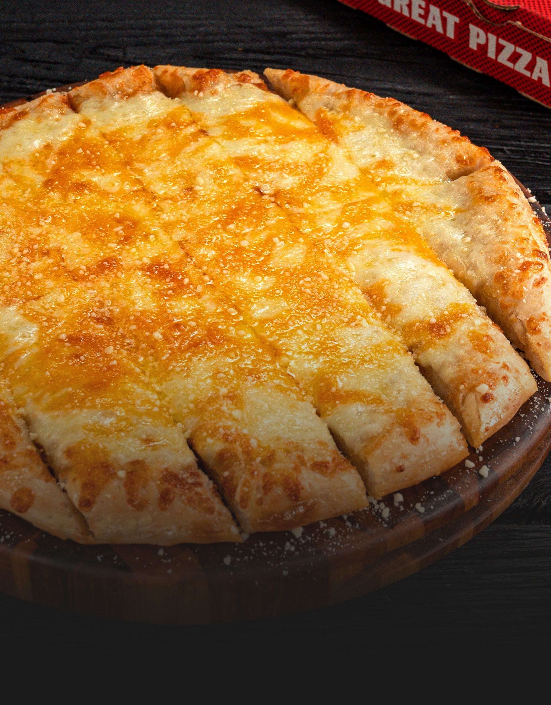 A pizza is sitting on a wooden cutting board next to a box that says great pizza.