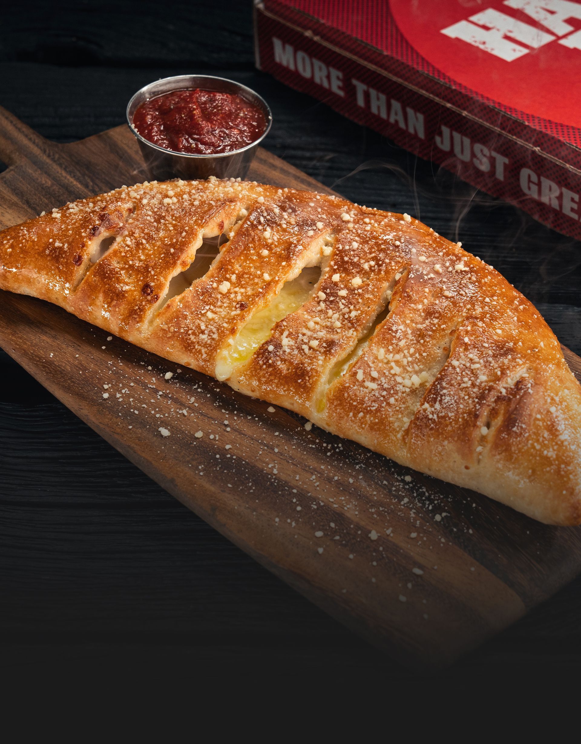 A calzone is sitting on a wooden cutting board next to a bowl of sauce.