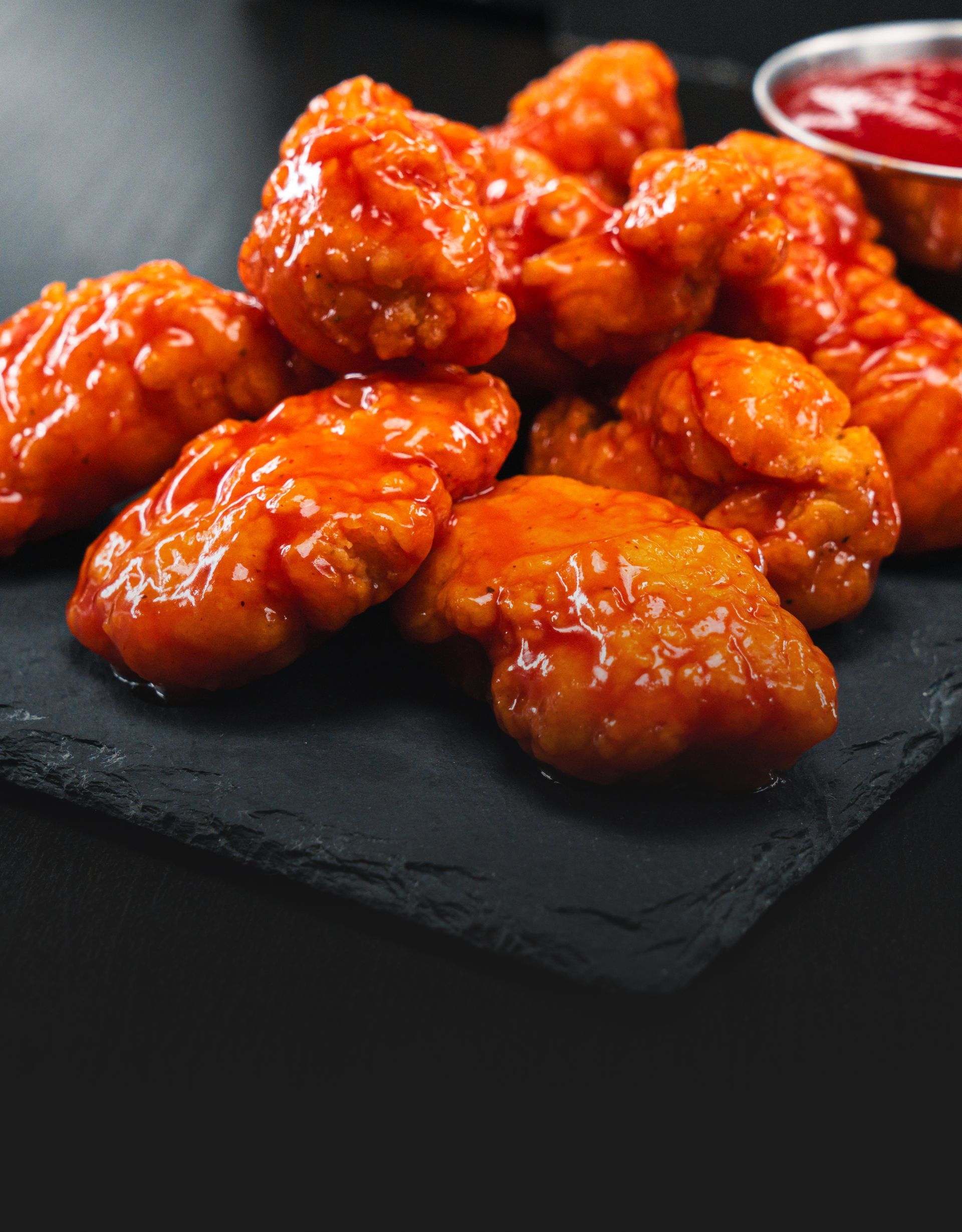 Crispy boneless chicken wings tossed in tangy buffalo sauce on a black platter.