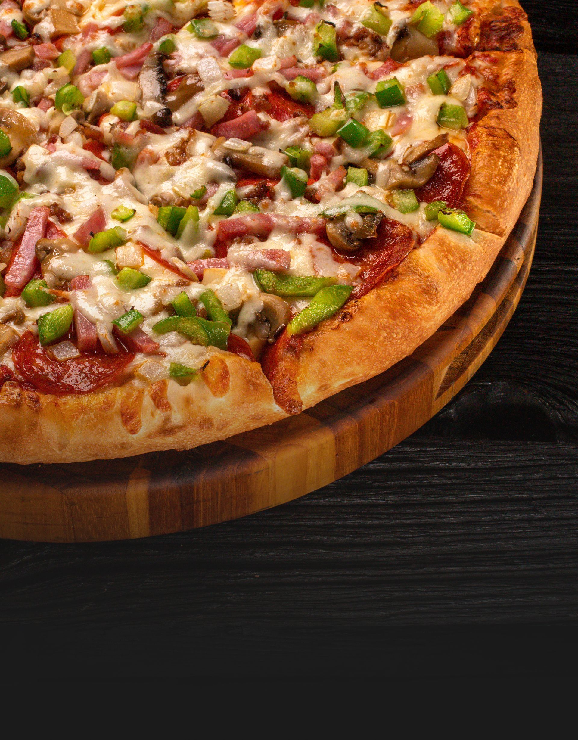 Everything pizza with green peppers, mushrooms, ham, and pepperoni on a wooden cutting board
