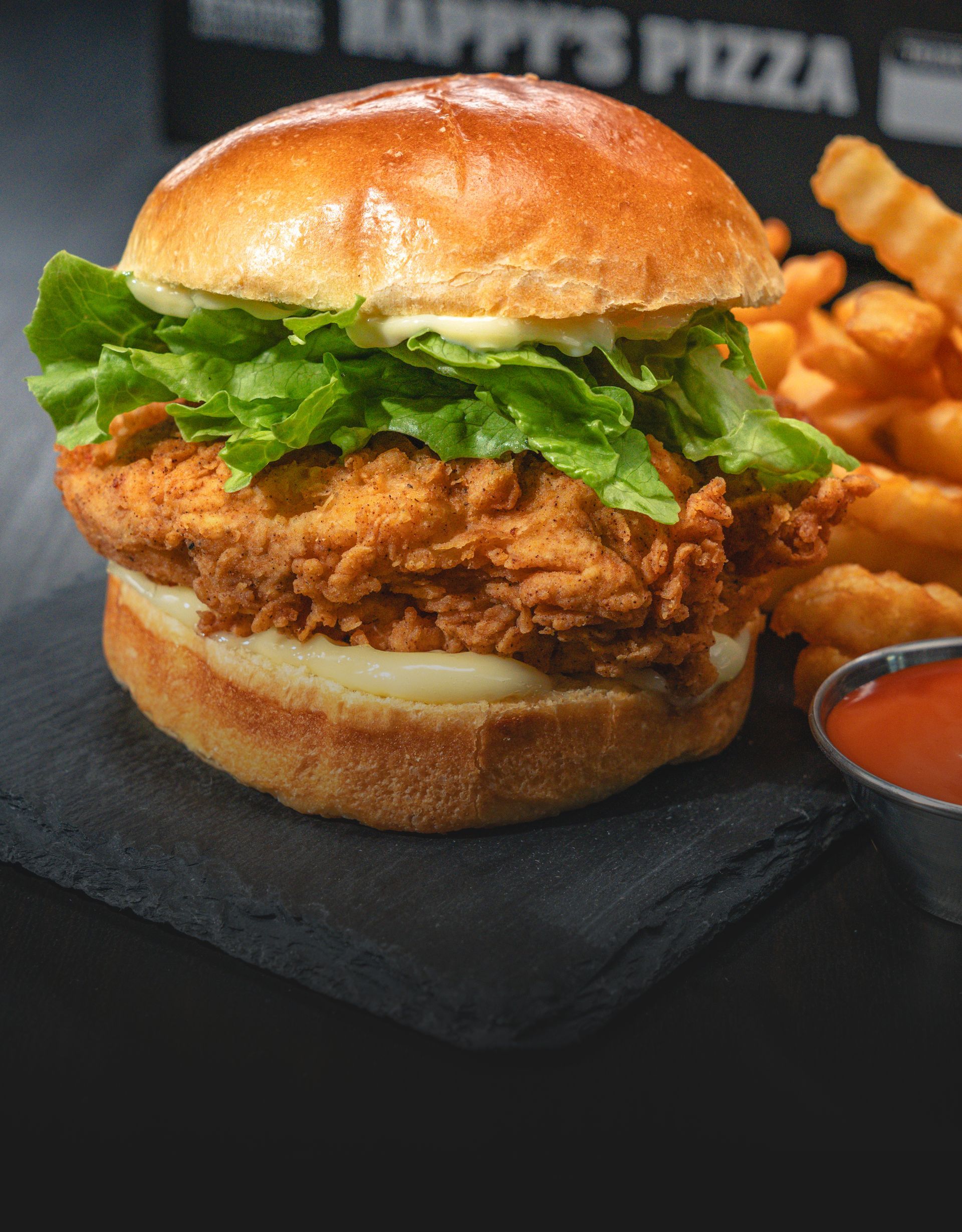 A chicken sandwich on a bun with lettuce and cheese next to french fries.