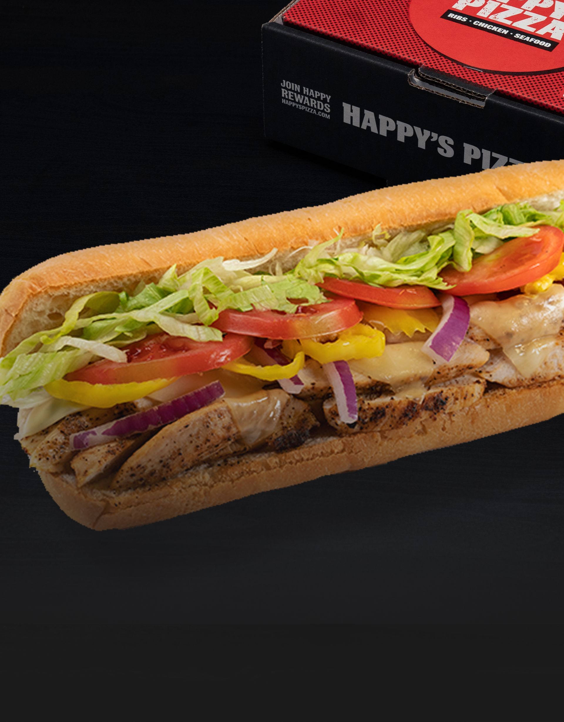 A sub sandwich with chicken , lettuce , tomatoes , peppers and onions is sitting on a table.