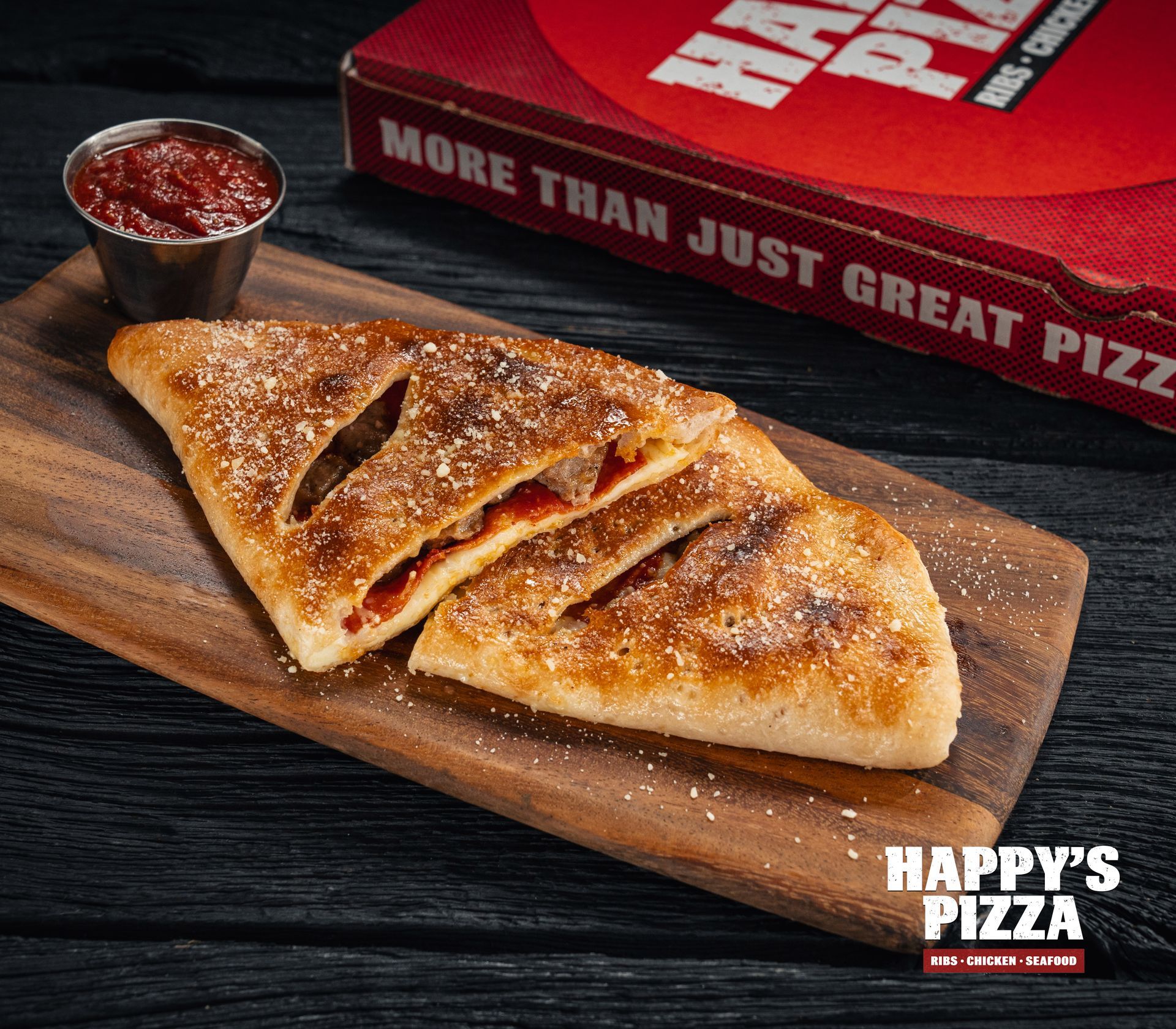 A pizza sitting on a wooden cutting board next to a box that says happy 's pizza