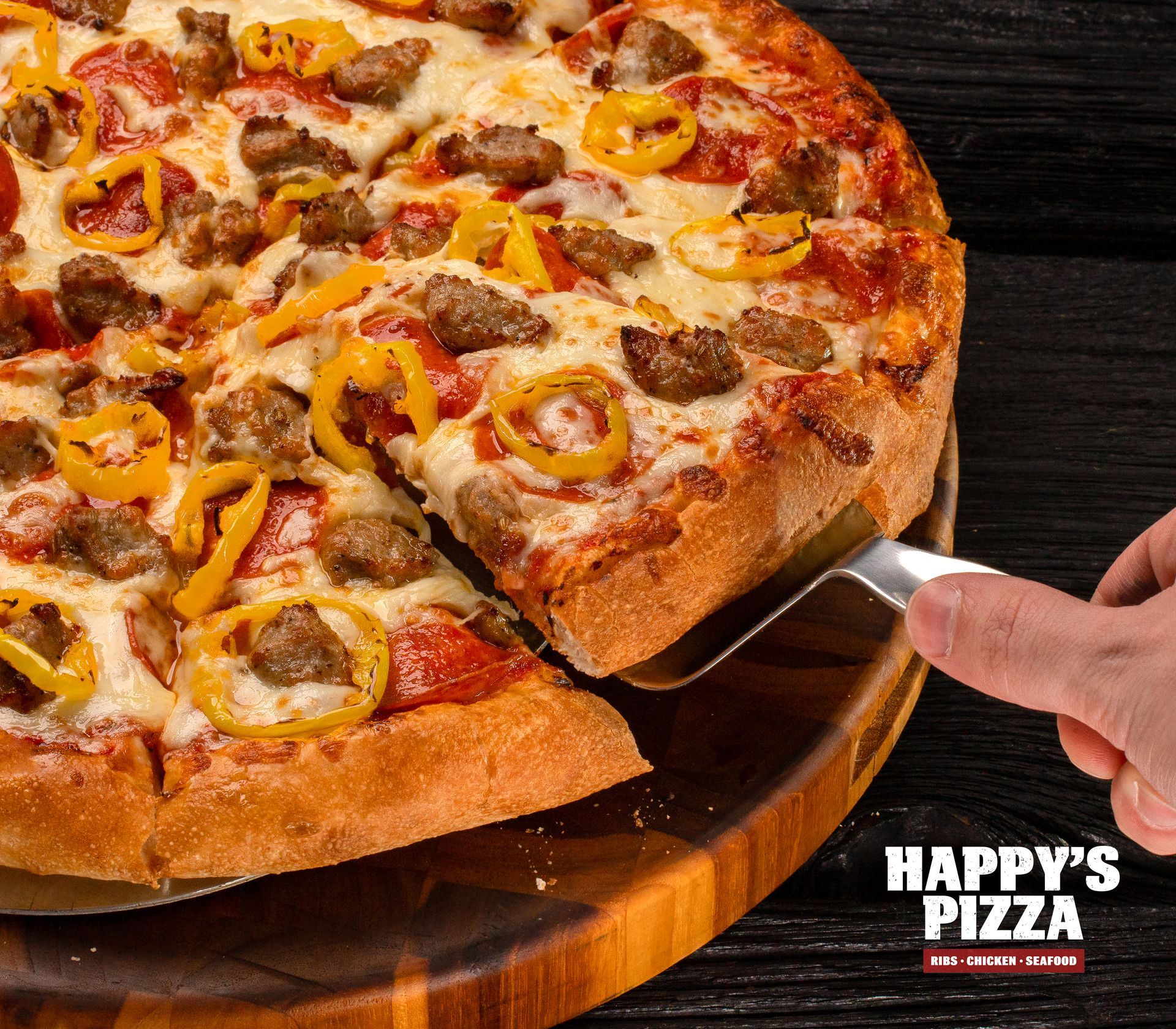 A person is cutting a pizza with a spatula from happy 's pizza