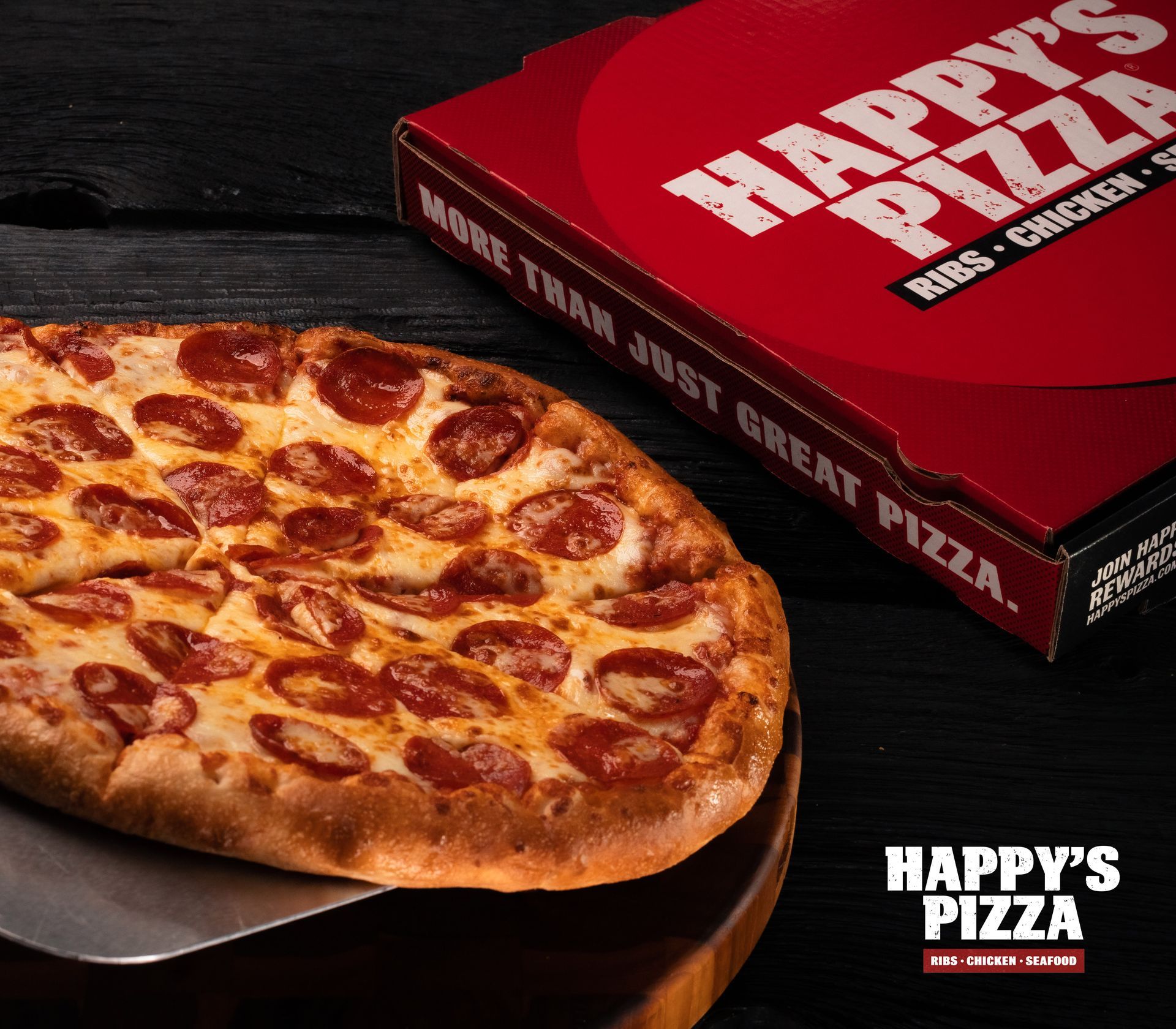 A pepperoni pizza next to a happy 's pizza box