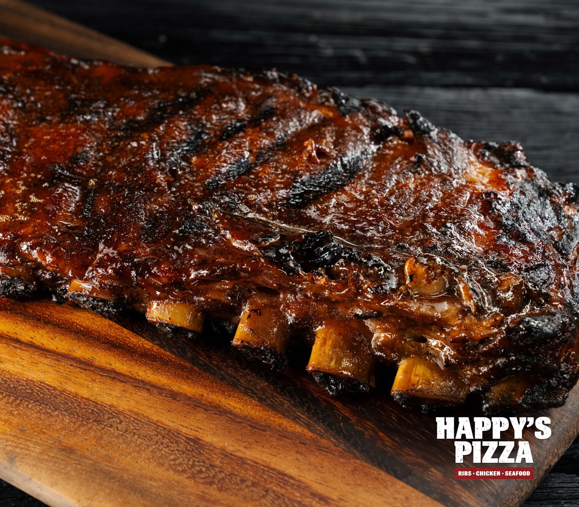 A large piece of meat is sitting on a wooden cutting board from happy 's pizza