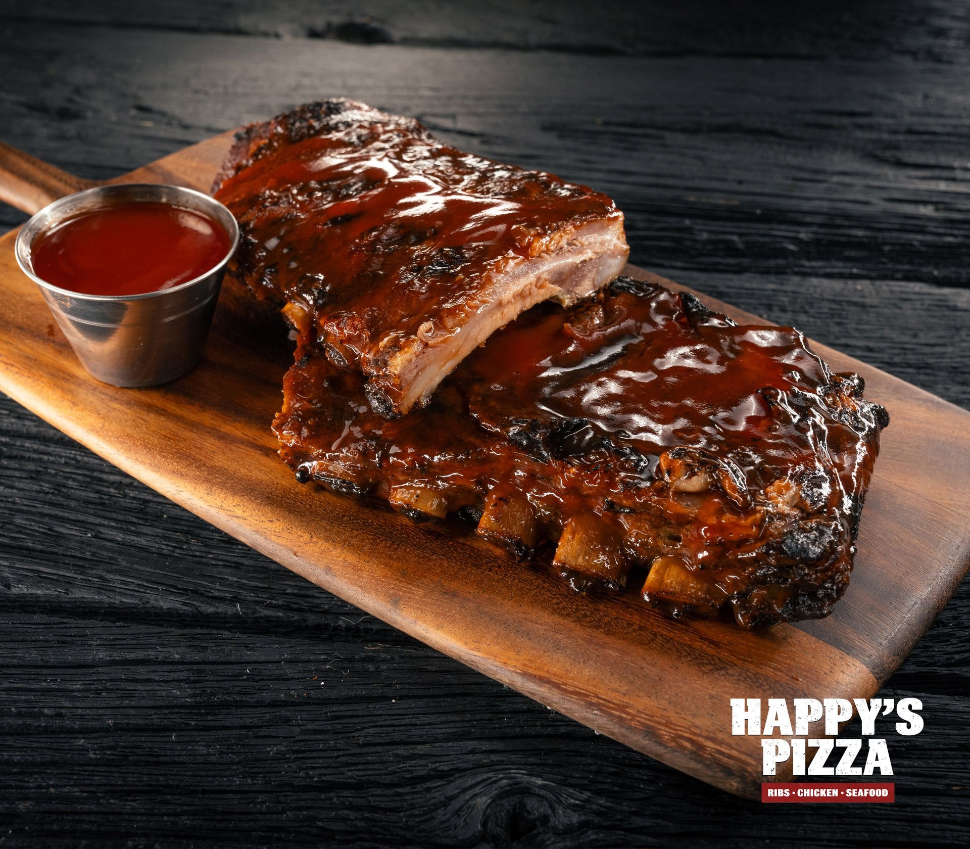 A wooden cutting board topped with ribs and ketchup.