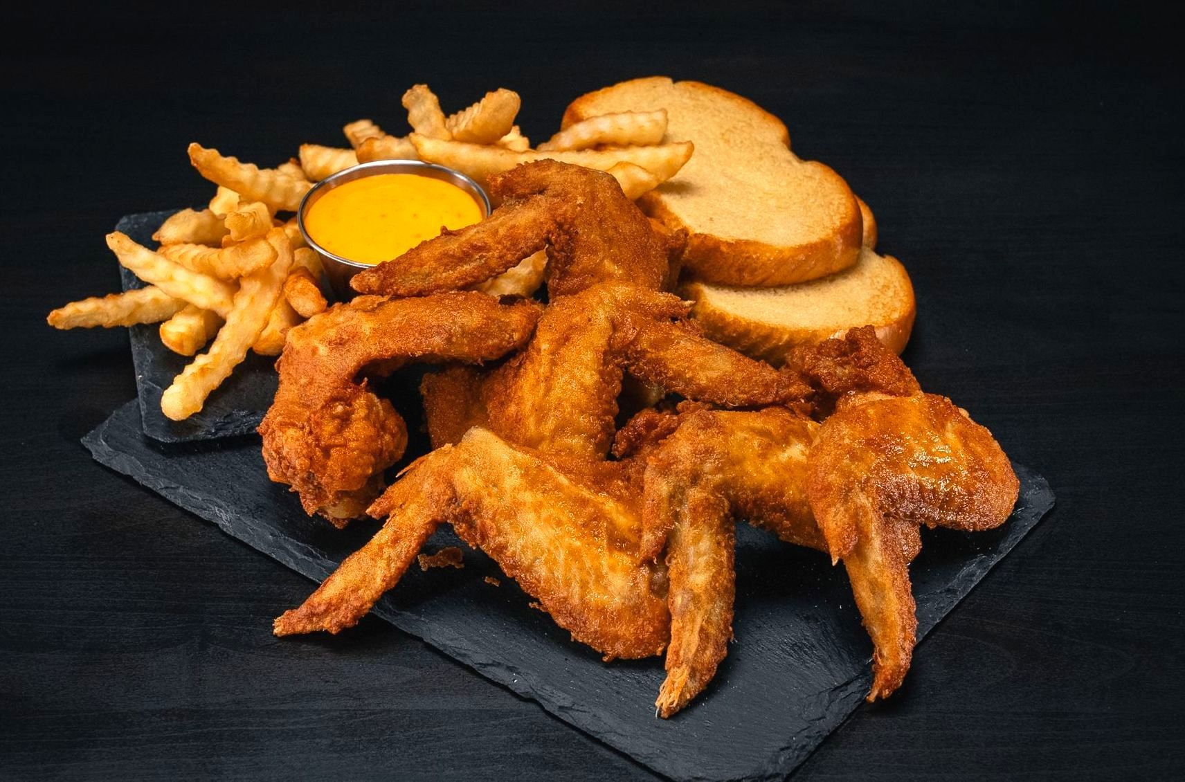 A tray of chicken wings , french fries , and bread on a table.